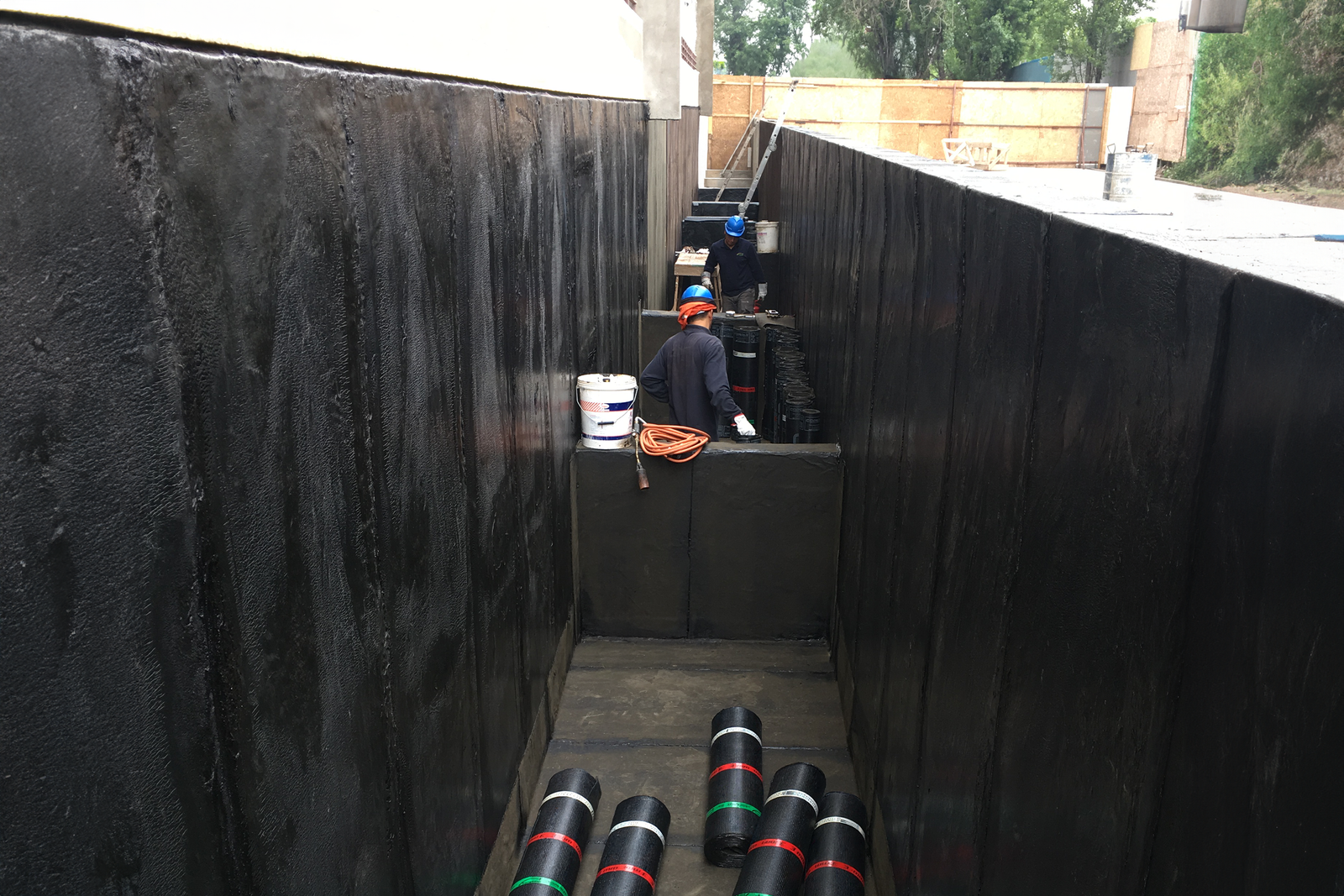 Trabajadores aplicando membrana asfáltica para impermeabilizar muros de contención y fundaciones