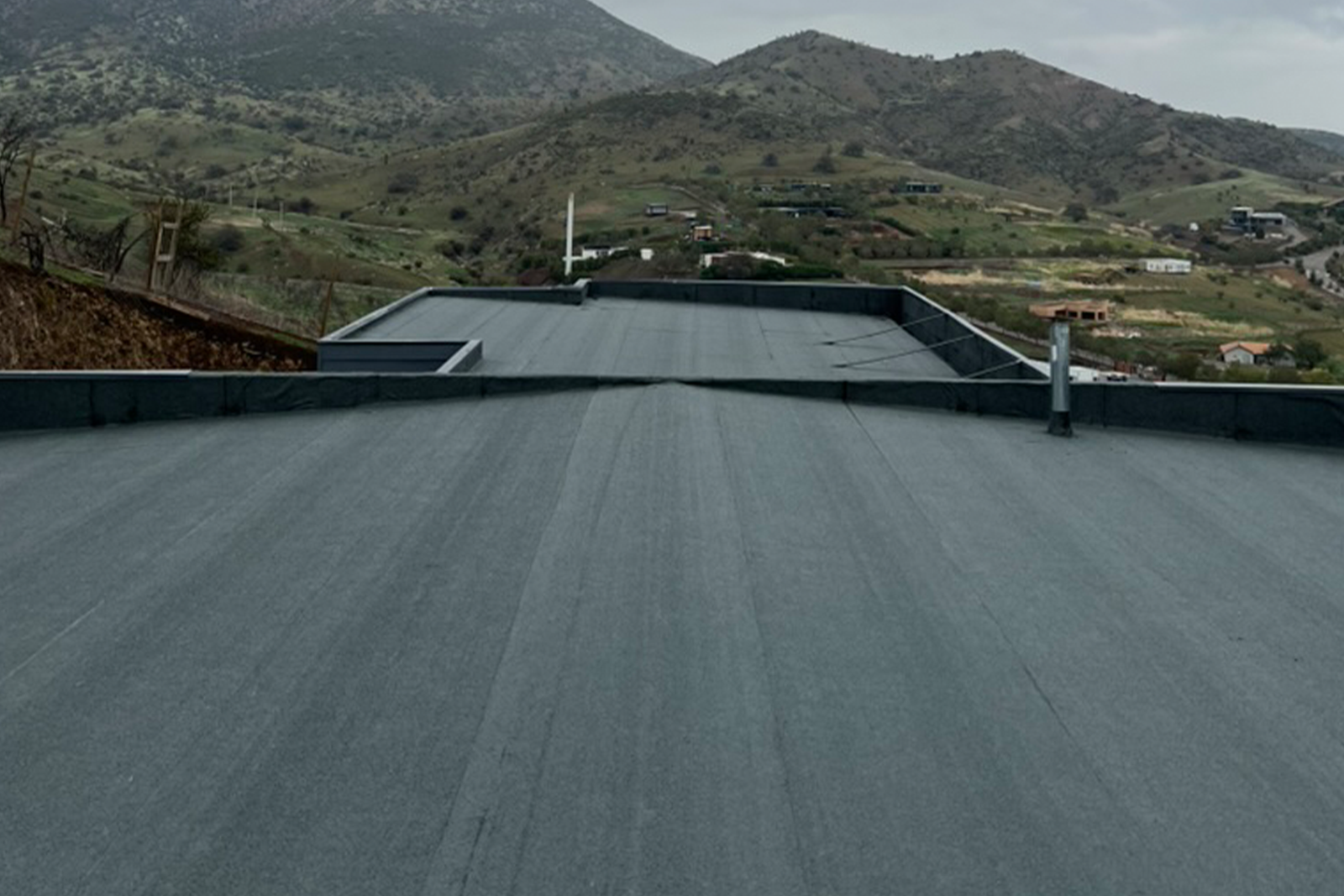 Cubierta impermeabilizada con membrana asfáltica gris en zona montañosa.