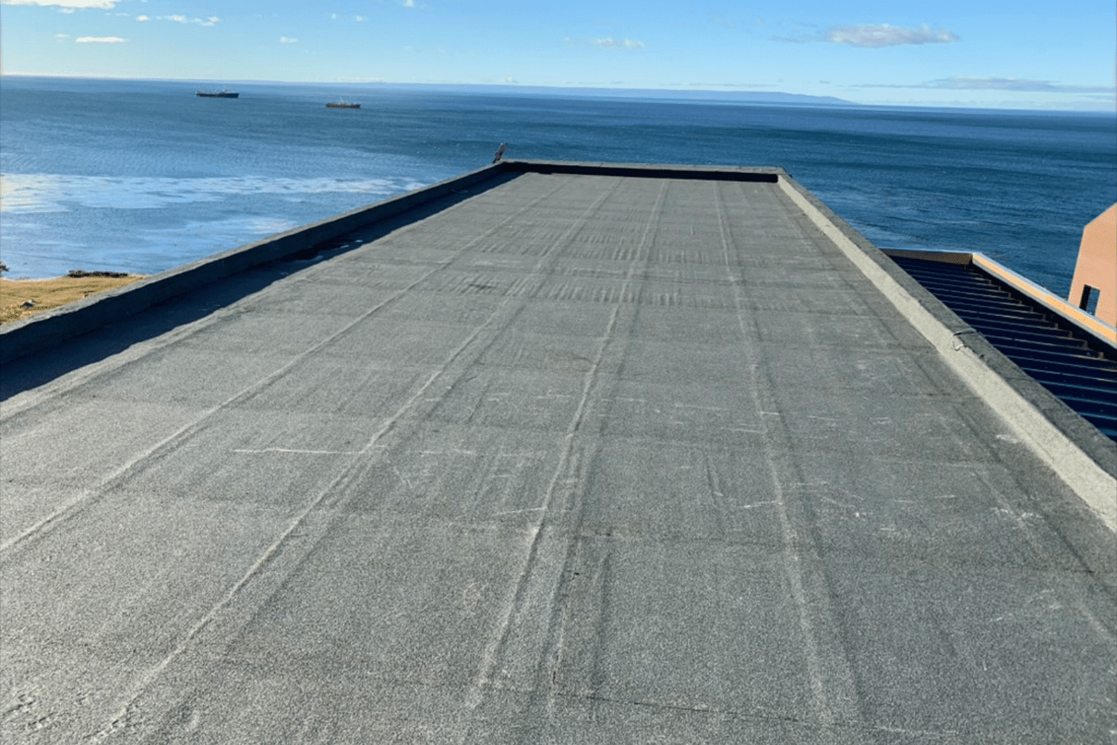 Cubierta impermeabilizada con membrana asfáltica gris en azotea frente al mar.