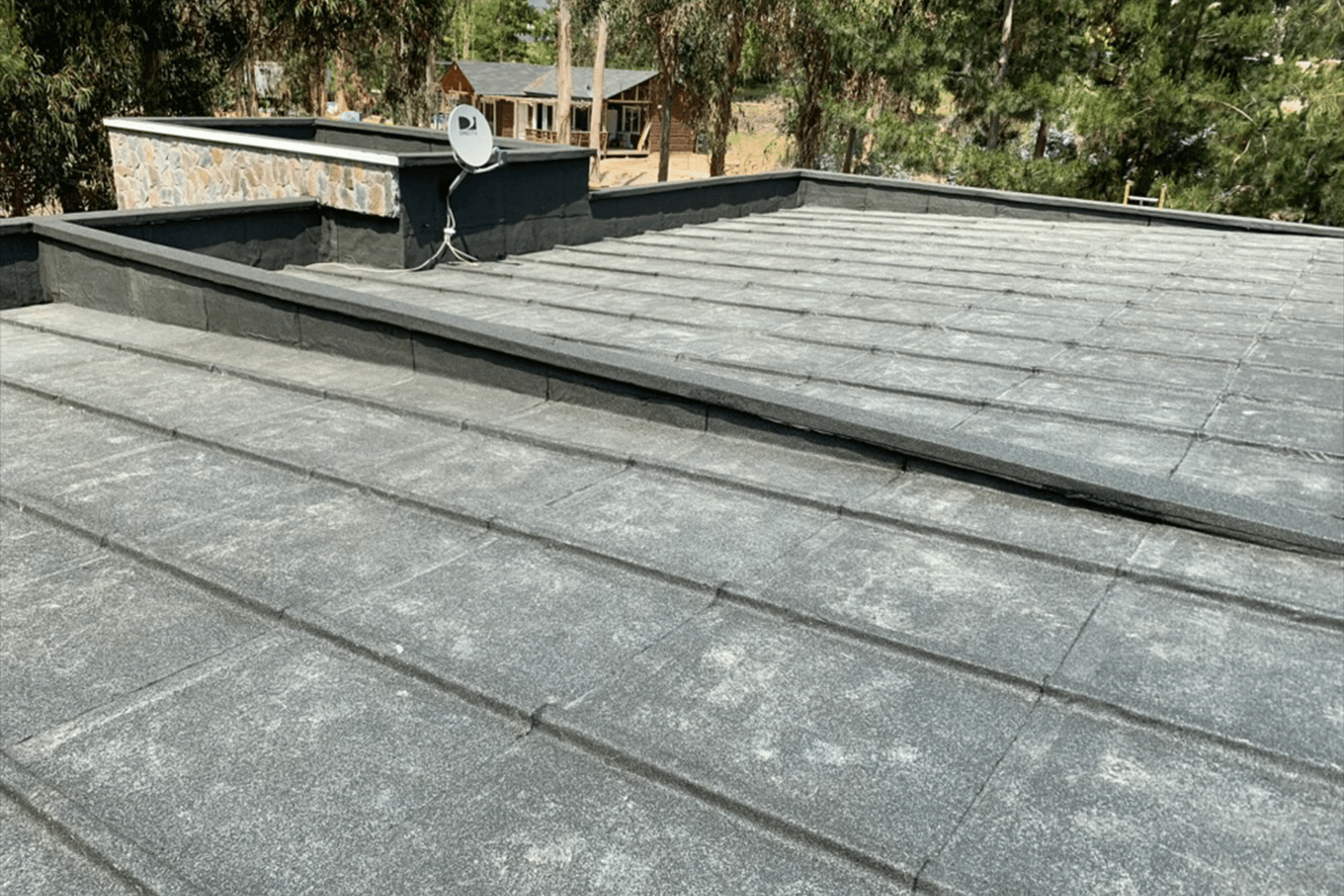 Cubierta plana impermeabilizada con membrana asfáltica en vivienda residencial rodeada de árboles.
