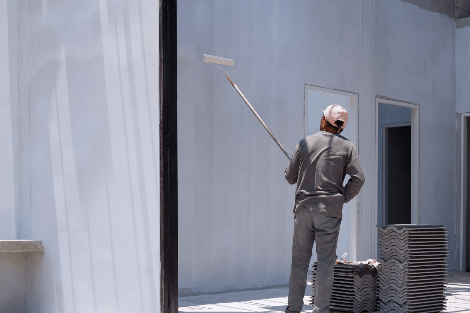 Trabajador pintando e impermeabilizando muro exterior con rodillo.